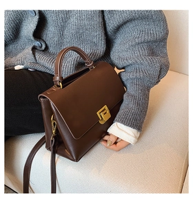 Detail of dark brown leather tote with gold lock carried by model on sofa