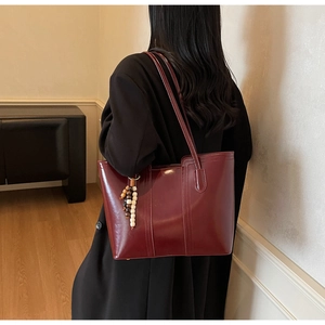 Detailed view of deep red glossy leather tote bag with a wooden bead charm on shoulder