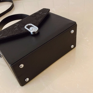 Detail of black rectangular box bag with snake pattern texture and silver metal lock
