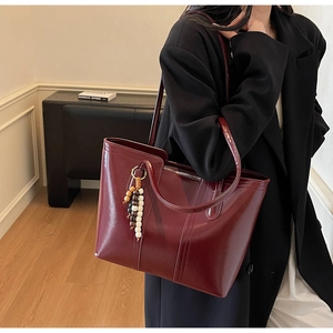 Detail of burgundy tote bag with glossy finish and stylish beaded keychain accessory
