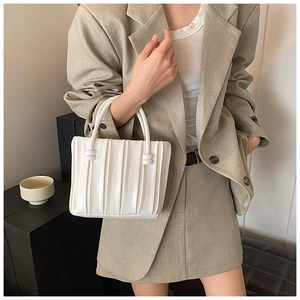 Detail of white pleated handbag with beaded handle and vertical stripe texture design
