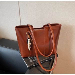 Close-up of brown leather tote bag with decorative stitching and beaded charm detail