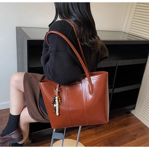 Detail of vintage brown tote bag showing smooth PU leather texture and beaded charm