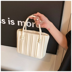 Detail of cream white pleated handbag with unique cylinder knot handle accents