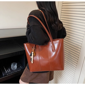 Detailed view of a brown leather tote bag with vertical stitching and beaded charm accessory