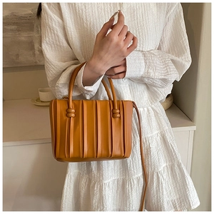 Detail view of orange pleated handbag with rounded handles and long shoulder strap