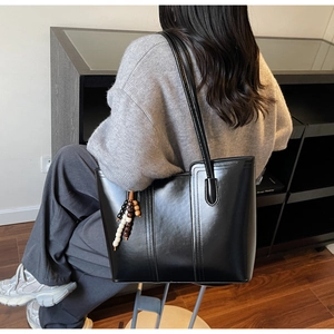 Glossy black tote bag with decorative stitching and colorful beaded charm on a shoulder strap
