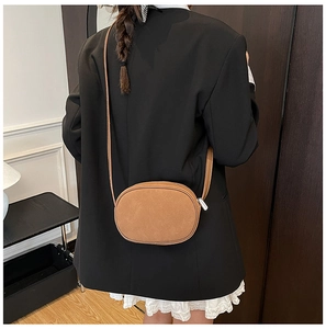 Close-up of a brown matte leather crossbody bag with a slim shoulder strap on a model