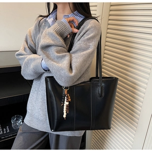 Detail of black leather tote bag with wooden bead charm worn over a grey sweater