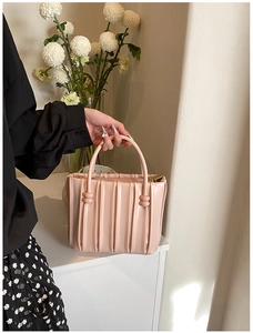 Detailed view of pink pleated handbag with a cylindrical handle and chic ring accents