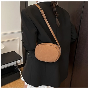 Side view of a brown oval crossbody bag showing adjustable strap and matte leather finish