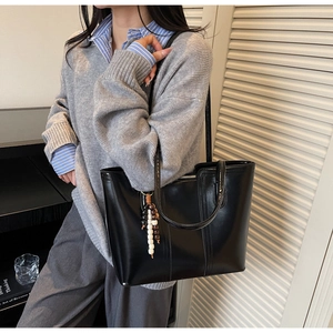 Detail of black PU leather tote bag with unique wood bead pendant and vertical stitching