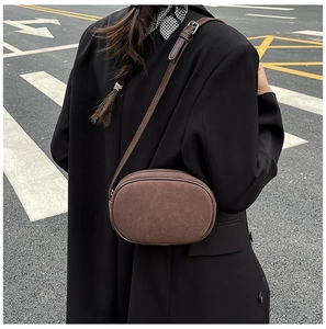 Detail of dark brown suede crossbody bag worn with a black blazer in a street setting