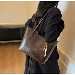 Detail of dark brown glossy tote bag with stylish vertical stitching and beaded tassel charm