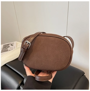 Detail of a brown oval crossbody bag with suede texture and silver buckle adjustment