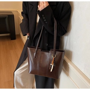 Detail of vintage brown tote bag featuring glossy texture and colorful beaded charm accessory