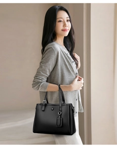 Détail d'un sac à main noir en cuir à motif litchi avec des poignées rondes en métal