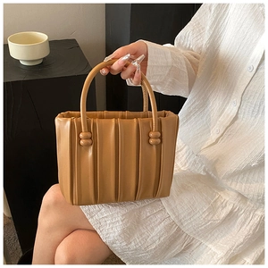 Detail of caramel pleated handbag with curved top handle and spherical decorative hardware
