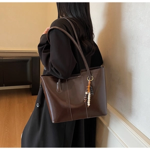 Detail of dark brown tote bag with glossy finish and wooden beaded charm on shoulder