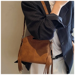Close-up of brown suede shoulder bag with long fringes and wide strap worn by a model