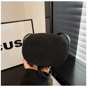 Detail of black suede oval crossbody bag with smooth leather trim and adjustable metal buckle