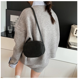 Minimalist black oval crossbody bag in matte finish styled with grey knitwear