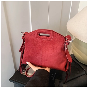Detail of red suede-textured handbag featuring stylish side tassels and cutout handle