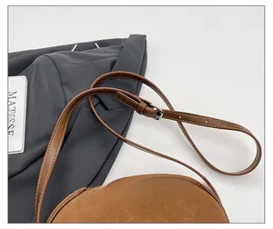 Detail view of brown suede crossbody bag showing the adjustable leather shoulder strap buckle