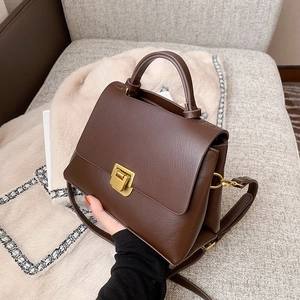Vintage dark brown leather crossbody handbag with metal buckle on a cozy sofa background