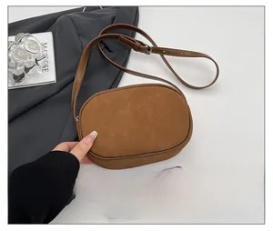 Minimalist brown suede crossbody bag with adjustable strap shown next to a smartphone