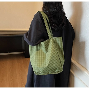 Detail shot of a large green and white checkered canvas tote bag worn by a model