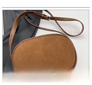 Close-up of brown suede crossbody bag showing textured fabric and silver buckle detail