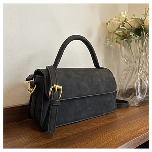 Détail du sac bandoulière noir mat avec côtés en accordéon et garniture dorée sur bois