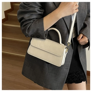 Sac bandoulière rectangulaire blanc cassé chic porté avec un blazer gris élégant