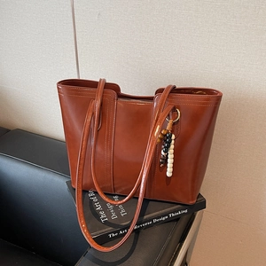 Vintage caramel brown leather tote bag with bead tassel charm on a black sofa