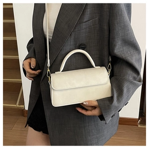 Sac à bandoulière chic en cuir crème avec poignée porté sur une veste de costume grise