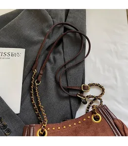 Detail of brown suede shoulder bag with gold studs and woven metal chain strap