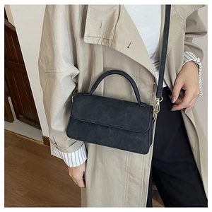 Détail d'un sac à main noir mat avec crochets dorés porté sur un trench-coat beige