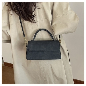 Détail d'un sac à main noir mat vintage porté avec un trench-coat beige élégant
