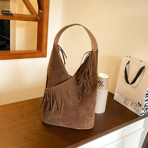 Borsa hobo in pelle scamosciata marrone con frange su un bancone di legno e caffè