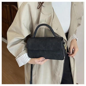 Détail d'un sac bandoulière noir mat avec poignée incurvée et boucles métalliques