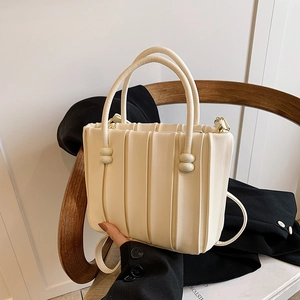Chic cream pleated handbag with round handles and gold hardware shown in a lifestyle setting