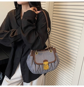 Detail of blue denim pleated shoulder bag with vintage gold clasp and leather strap
