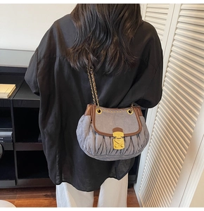 Detail of pleated denim-blue bag with leather trim and gold chain strap on model