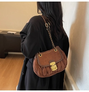 Close-up of brown suede shoulder bag featuring pleated texture and gold metal clasp