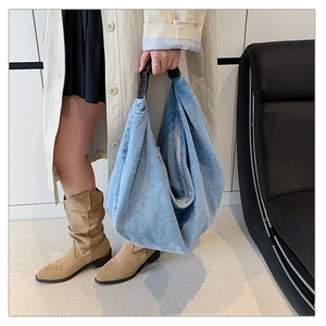 Blue denim crossbody shoulder bag styled with trench coat and brown boots in minimal room