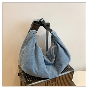 Detail of blue denim shoulder bag with adjustable buckle strap on black suitcase