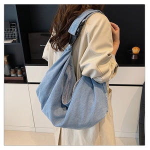 Detail of light blue denim tote bag with black adjustable strap and buckle closure