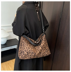 Detail view of a large leopard print tote bag with black leather straps on model