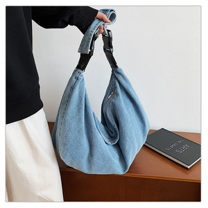 Detail of light blue denim tote bag with adjustable black buckle strap and metal zipper